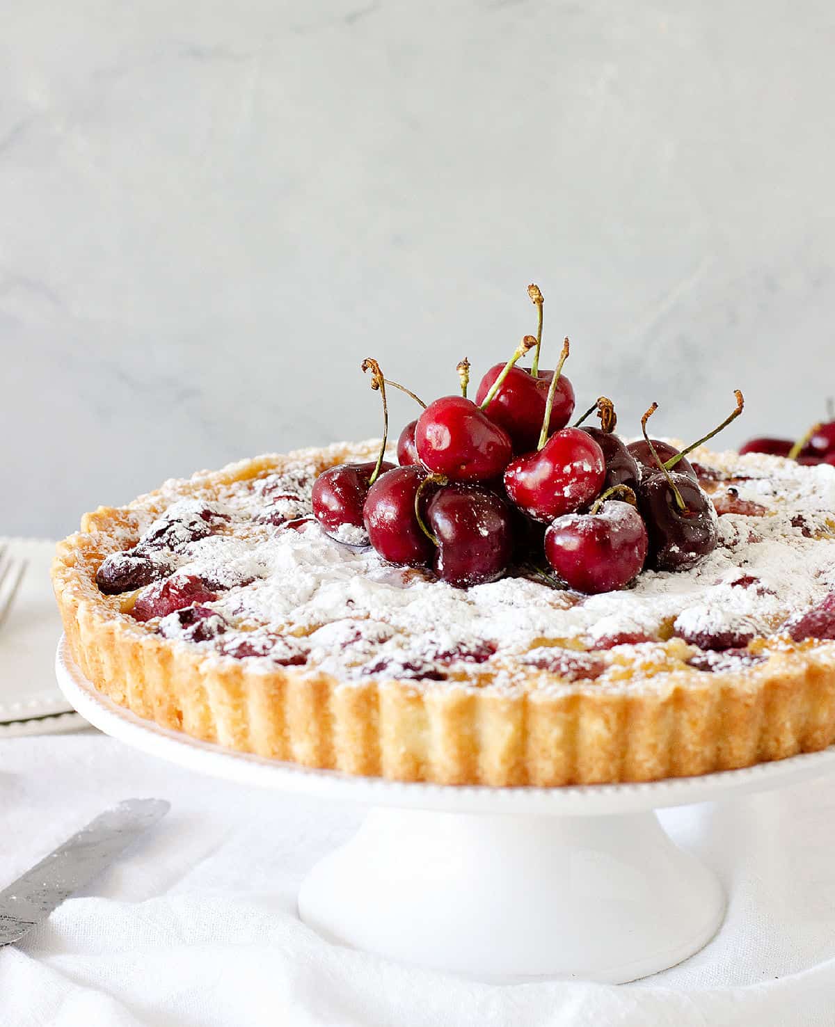 Whole cherry tart on a white pie plate with grey background.