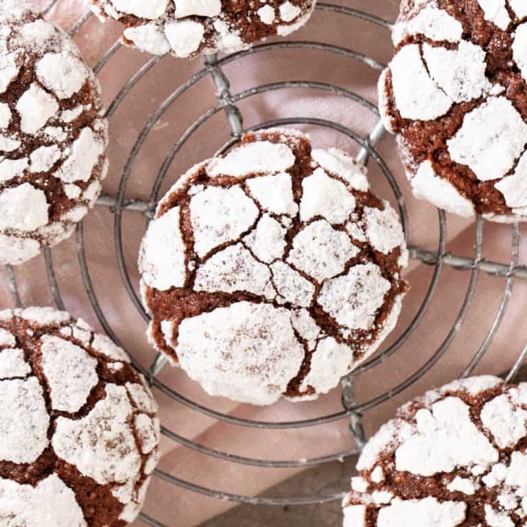 Several chocolate crinkle cookies on a wire rack with pink cloth underneath. Top view.
