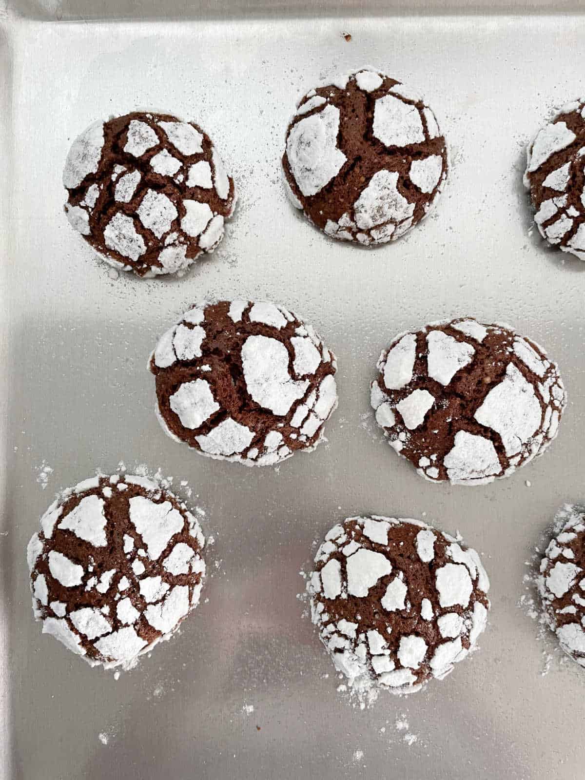 Chocolate crinkle cookies on a metal baking sheet. Top view. 