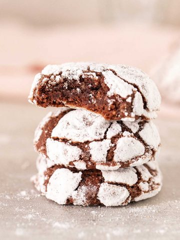 Pink background and grey surface with stack of chocolate crinkle cookies, top one bitten.