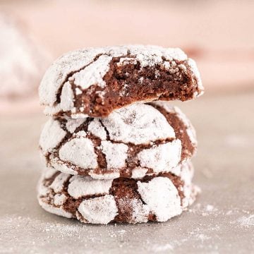Pink background and grey surface with stack of chocolate crinkle cookies, top one bitten.