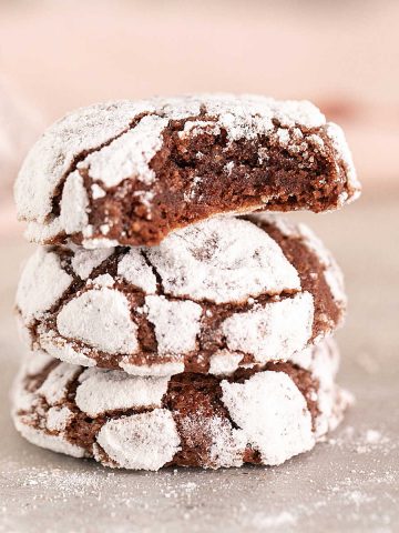 Pink background and grey surface with stack of chocolate crinkle cookies, top one bitten.