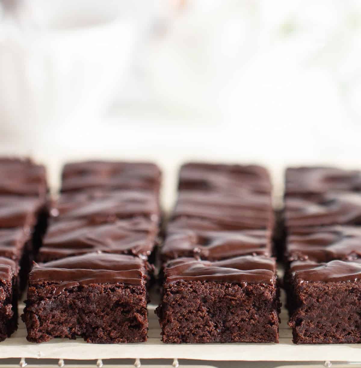 Rows of ganache topped brownie squares on parchment paper. White background.