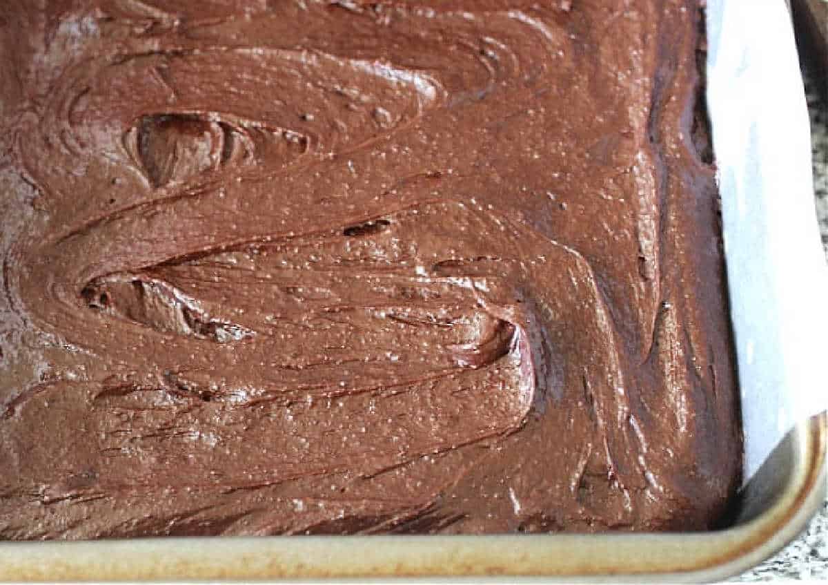 Unbaked brownie batter in metal pan with parchment paper.