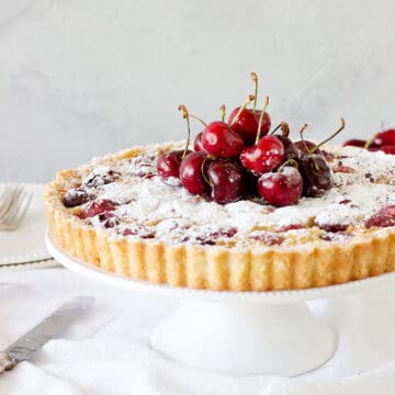 Front view of a cherry tart on a white cake stand, grey background.