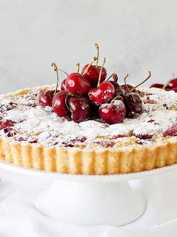 Front view of a cherry tart on a white cake stand, grey background.