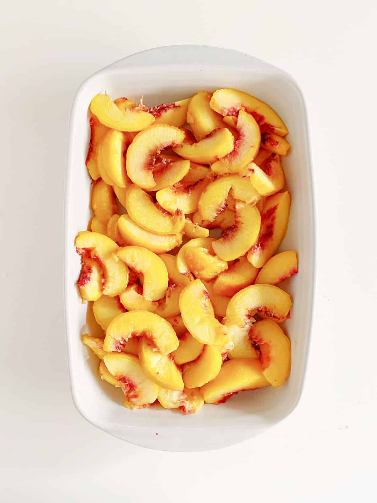 Top view of peach slices in rectangular white baking dish on a white surface.
