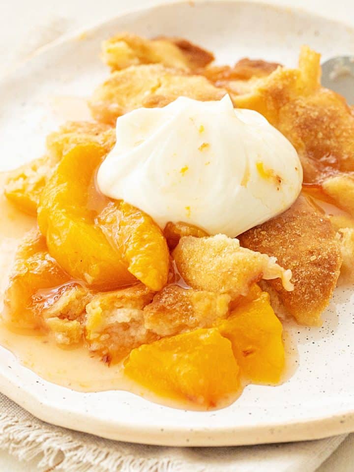 White plate with serving of peach cobbler with whipped cream.