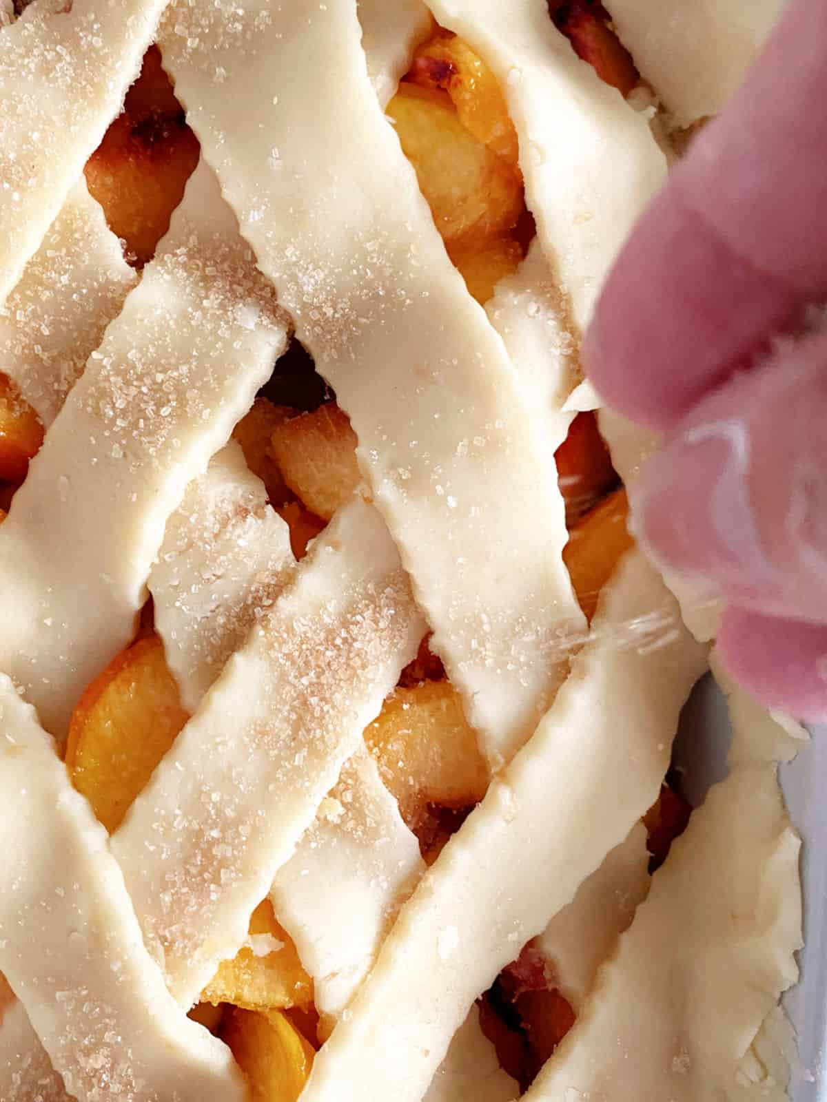 Hand sprinkling brown sugar on a lattice crust. Close up image.