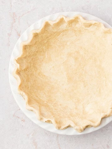 Crimpled all-butter pate brisee on a white pie dish. Marbled surface.