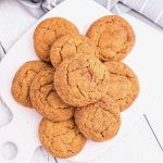 Top view of white board on a white surface with mound of pumpkin cookies.