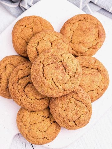 Top view of white board on a white surface with mound of pumpkin cookies.