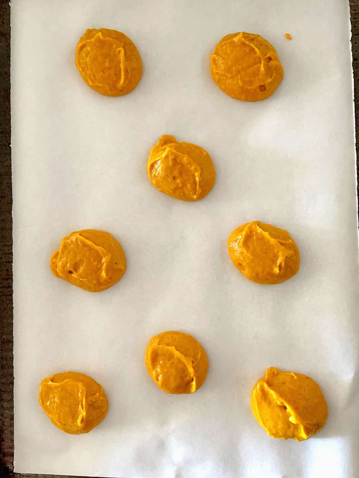 Several unbaked pumpkin cookies on white parchment paper on a cookie sheet.