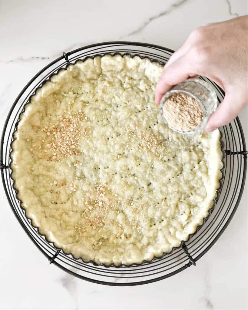 Sprinkling ground almonds on tart dough on a wire rack. White marble surface, top view.