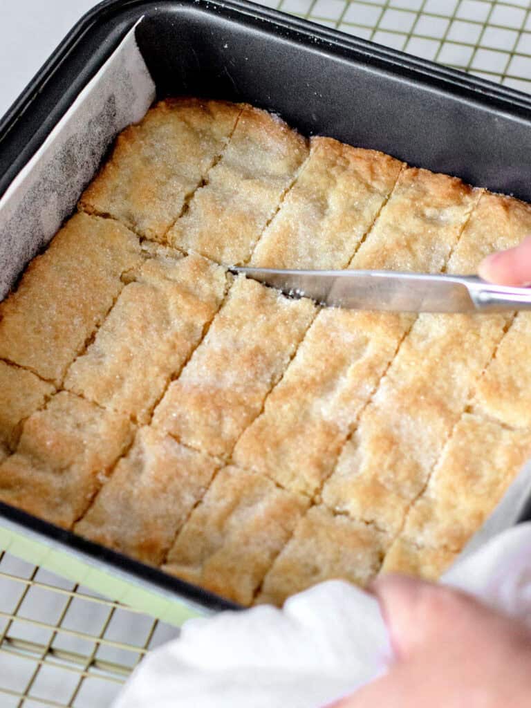 Scoring baked lemon shortbread in a dark metal pan.