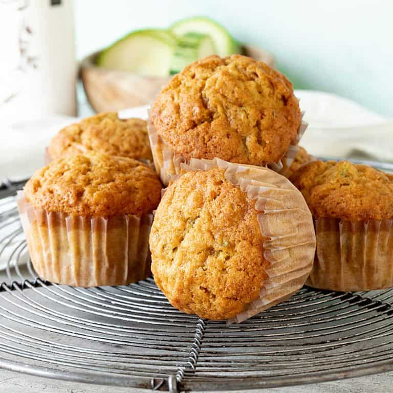Stacked pumpkin zucchini muffins in paper liners on a wire rack.