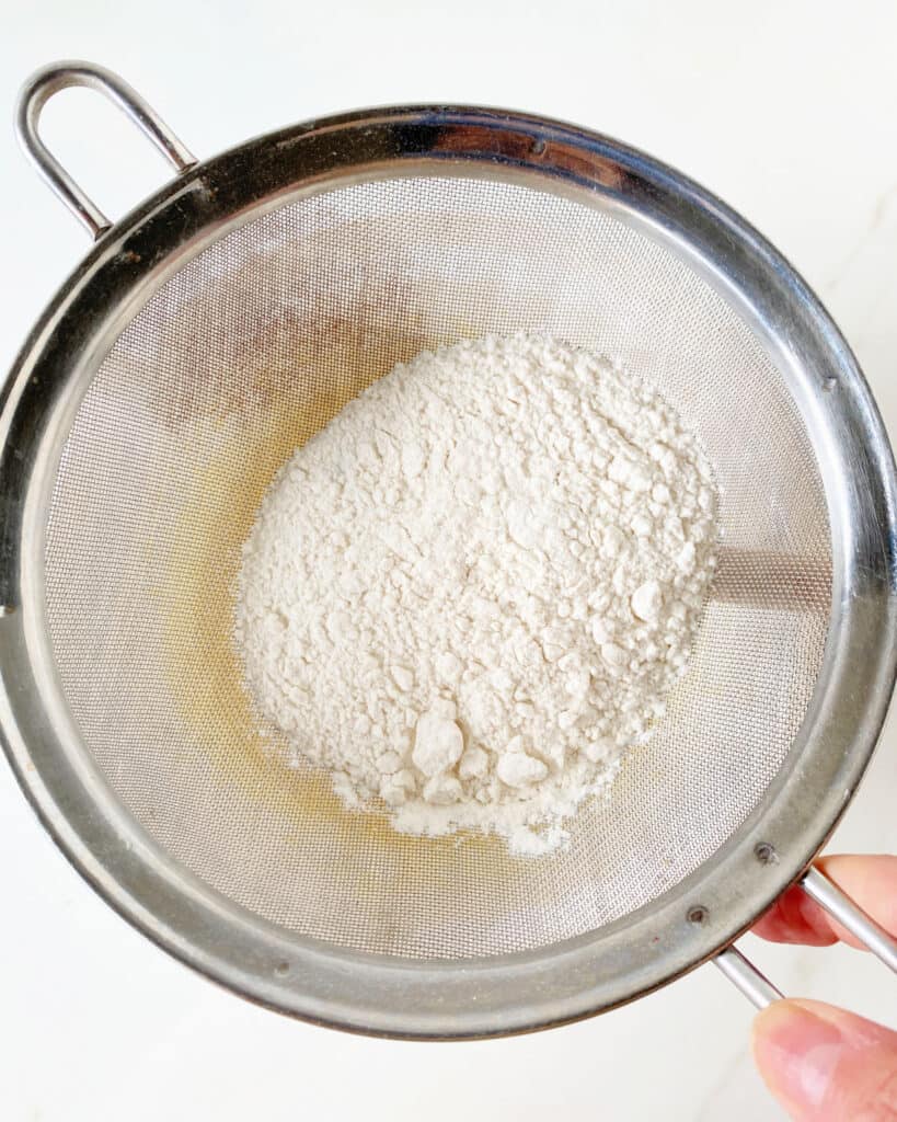 Sifting flour over cake batter with a metal mesh sifter.