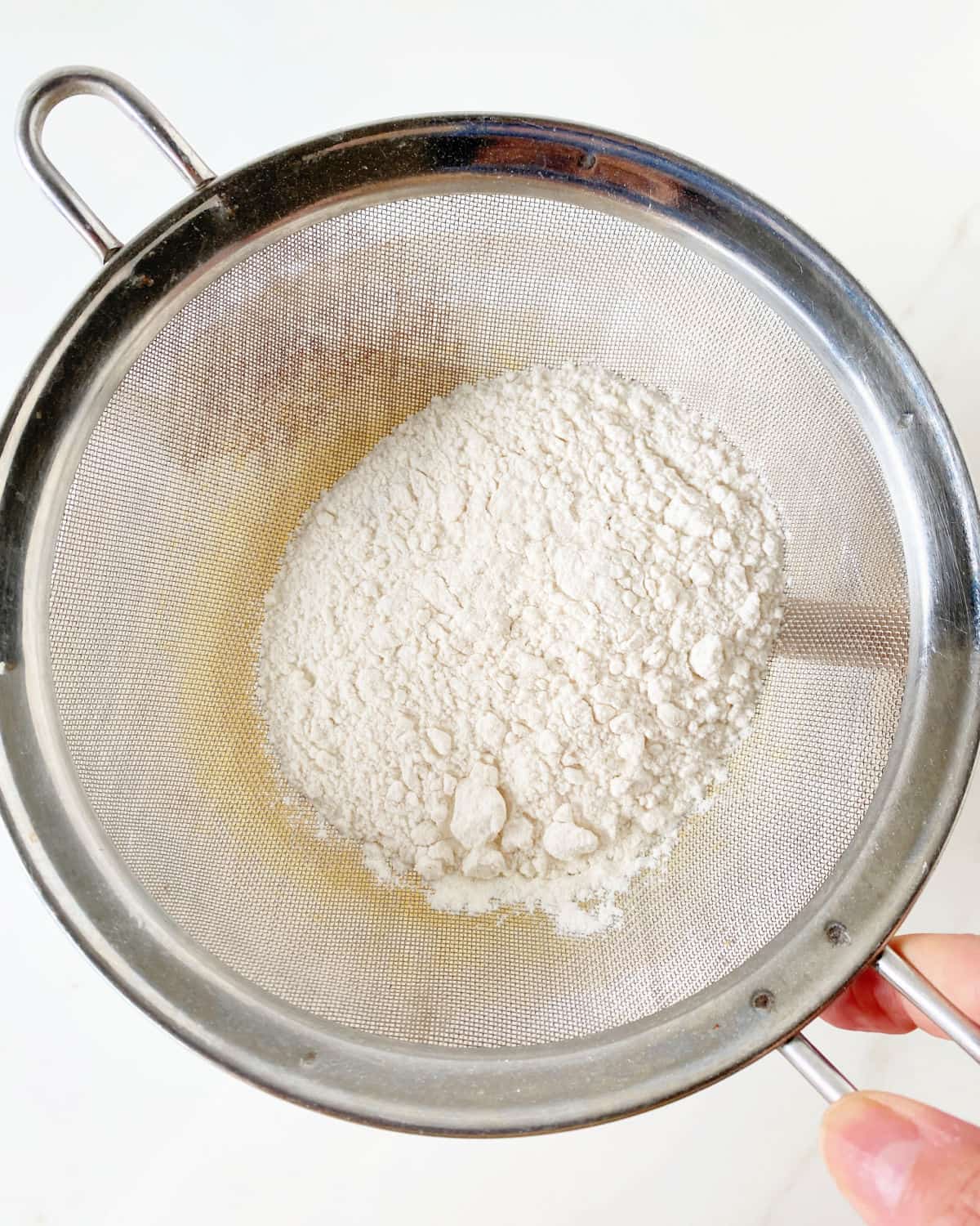 Sifting flour over cake batter with a metal mesh sifter.