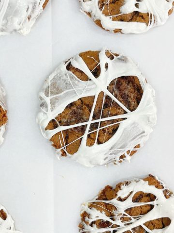 Flat top view of chocolate cookies with marshmallow webs on a white piece of paper.