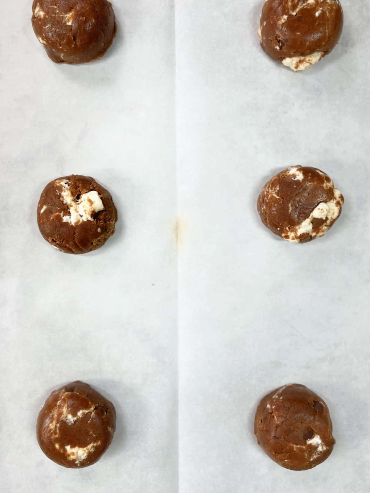 White parchment paper with chocolate marshmallow cookie dough balls. 