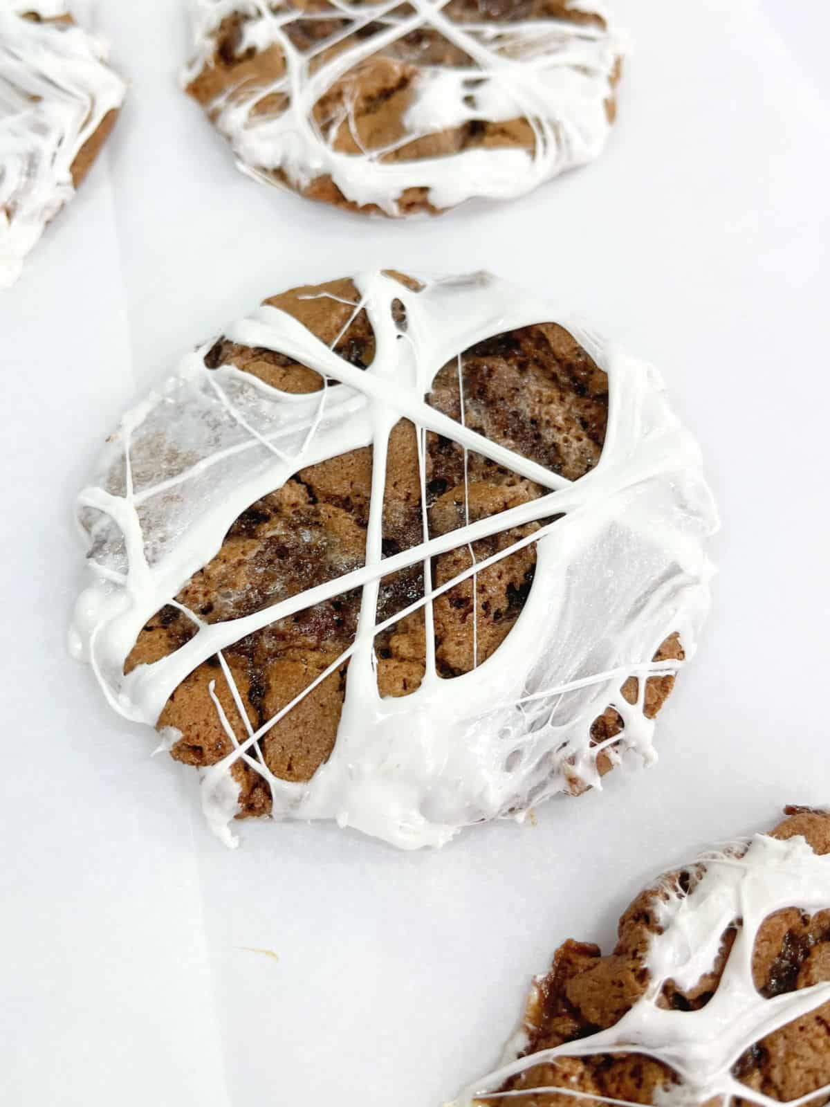 Spider web chocolate cookies on a white piece of parchment paper. 