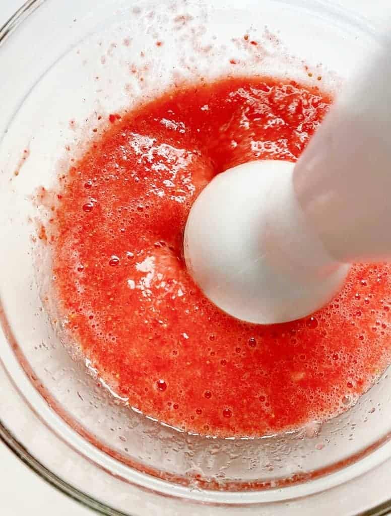 Strawberry puree in glass bowl with an immersion blender.