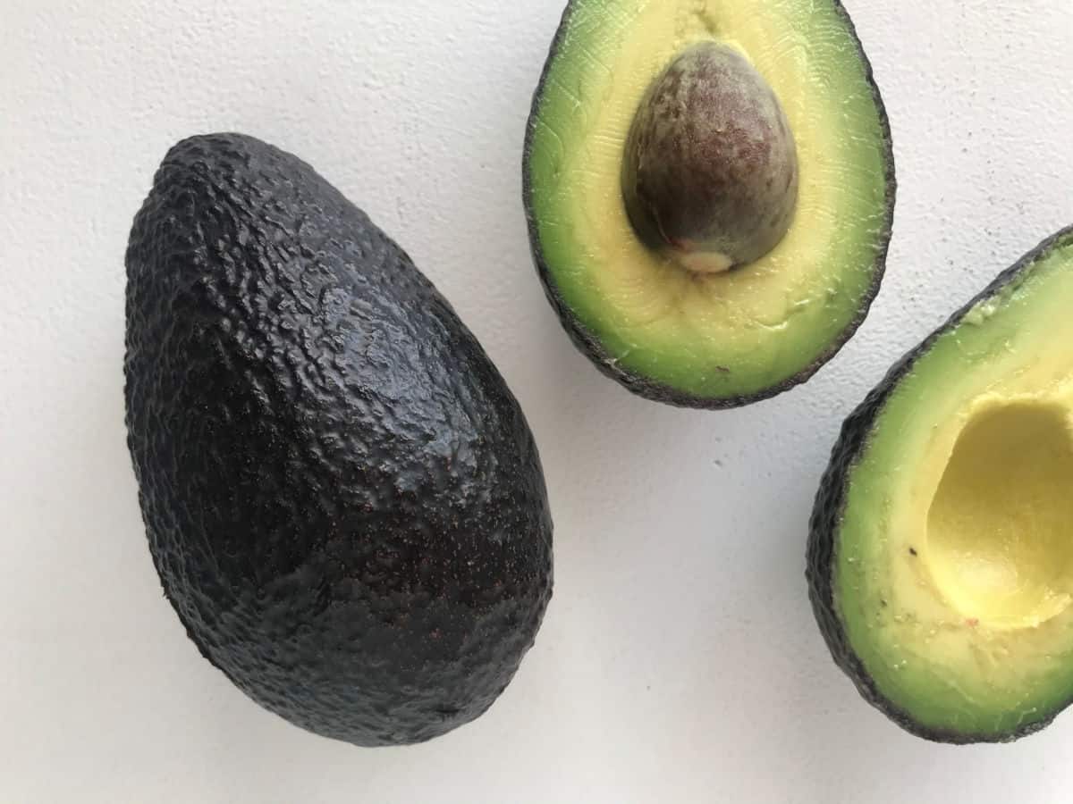 One whole avocado and two halved parts on a white surface.