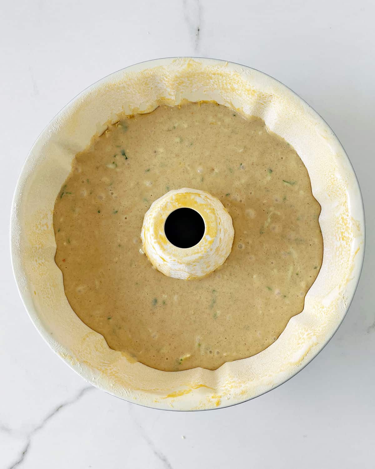 Cream-colored bundt pan with zucchini cake batter. White surface. Top view.