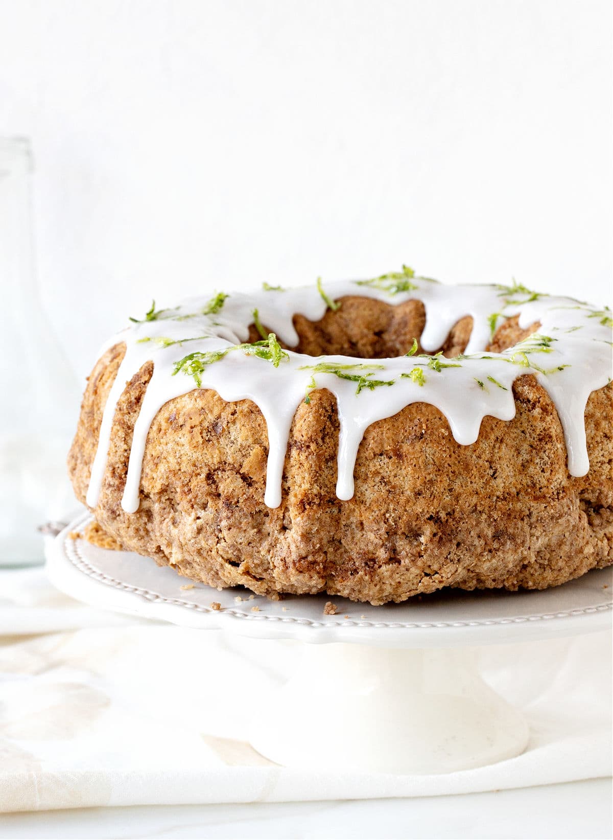 White background and white cake stand with glazed zucchini bundt cake.