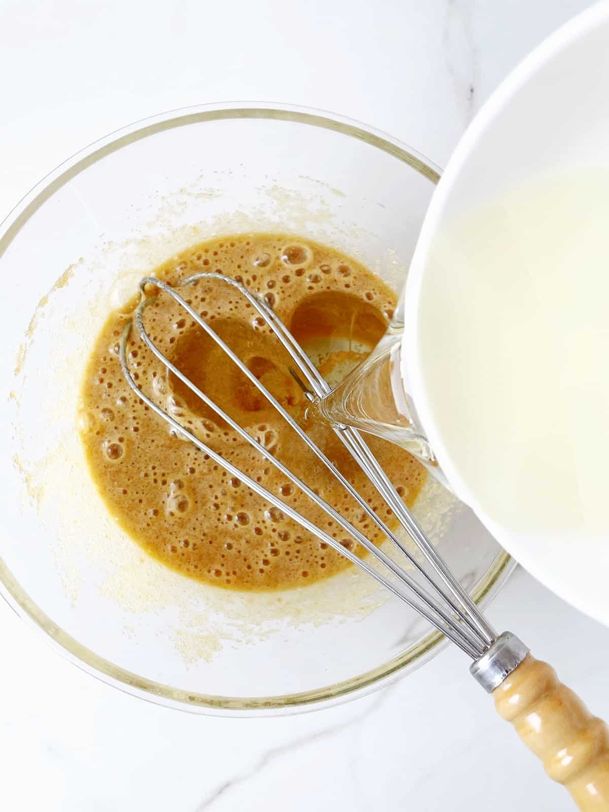 Adding oil to brown sugar muffin mixture in glass bowl with a whisk.