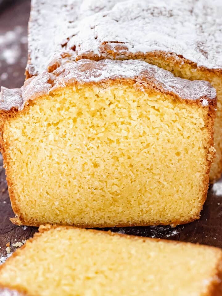 Loaf of brown butter pound cake with powdered sugar on a dark wooden board.