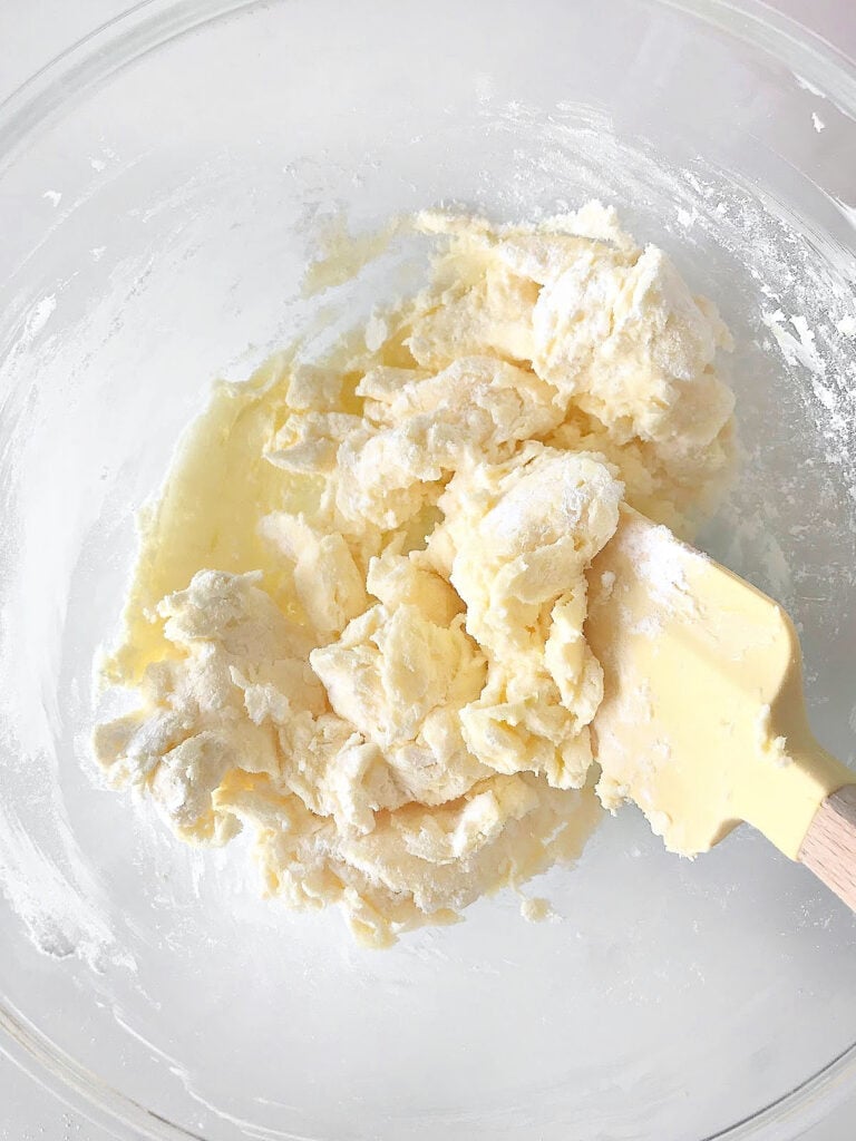 Integrating flour and butter with a yellow spatula. Glass bowl.