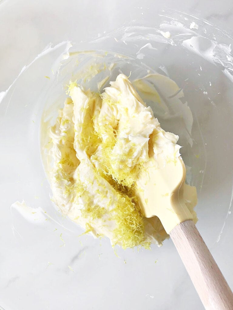Soft butter and lemon zest in a glass bowl. Yellow spatula.