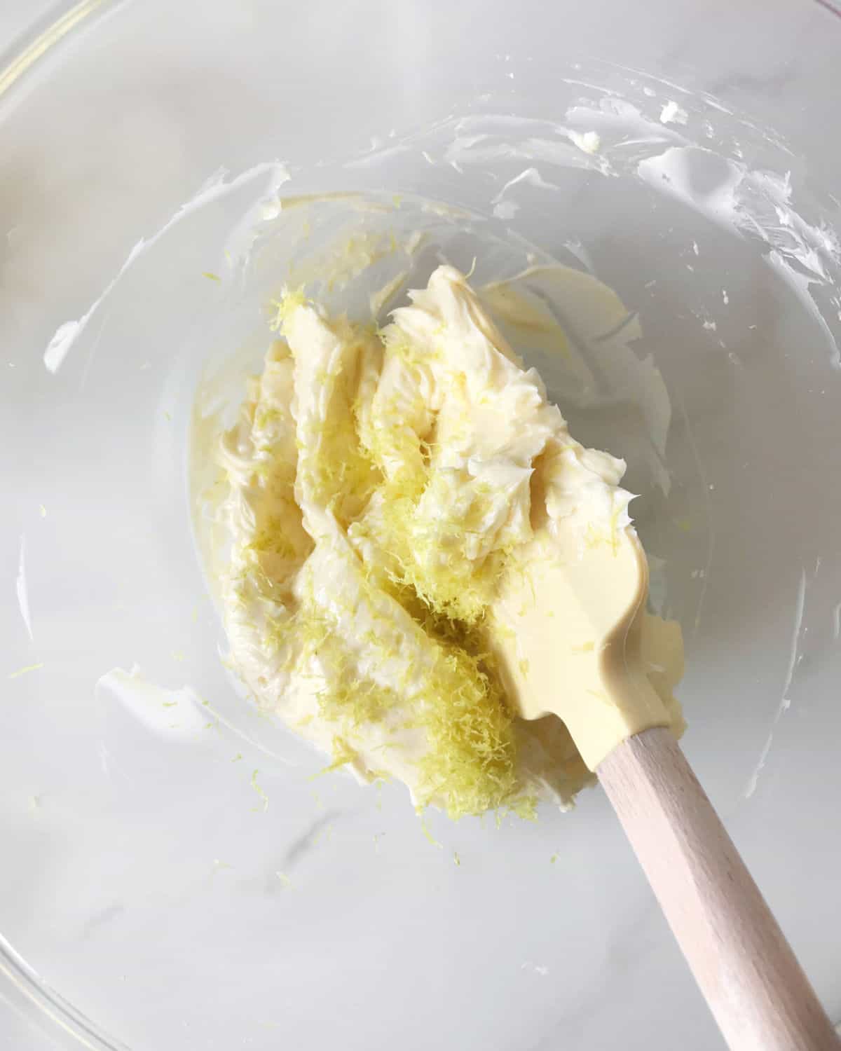 Lemon zest mixed with butter in a glass bowl with a yellow spatula. 