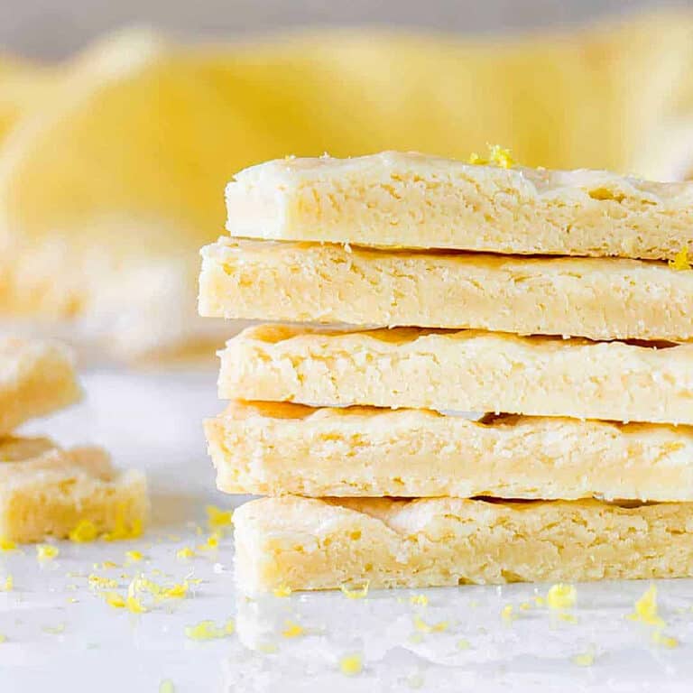 Stack of several lemon shortbread sticks with yellow background and white marble surface.