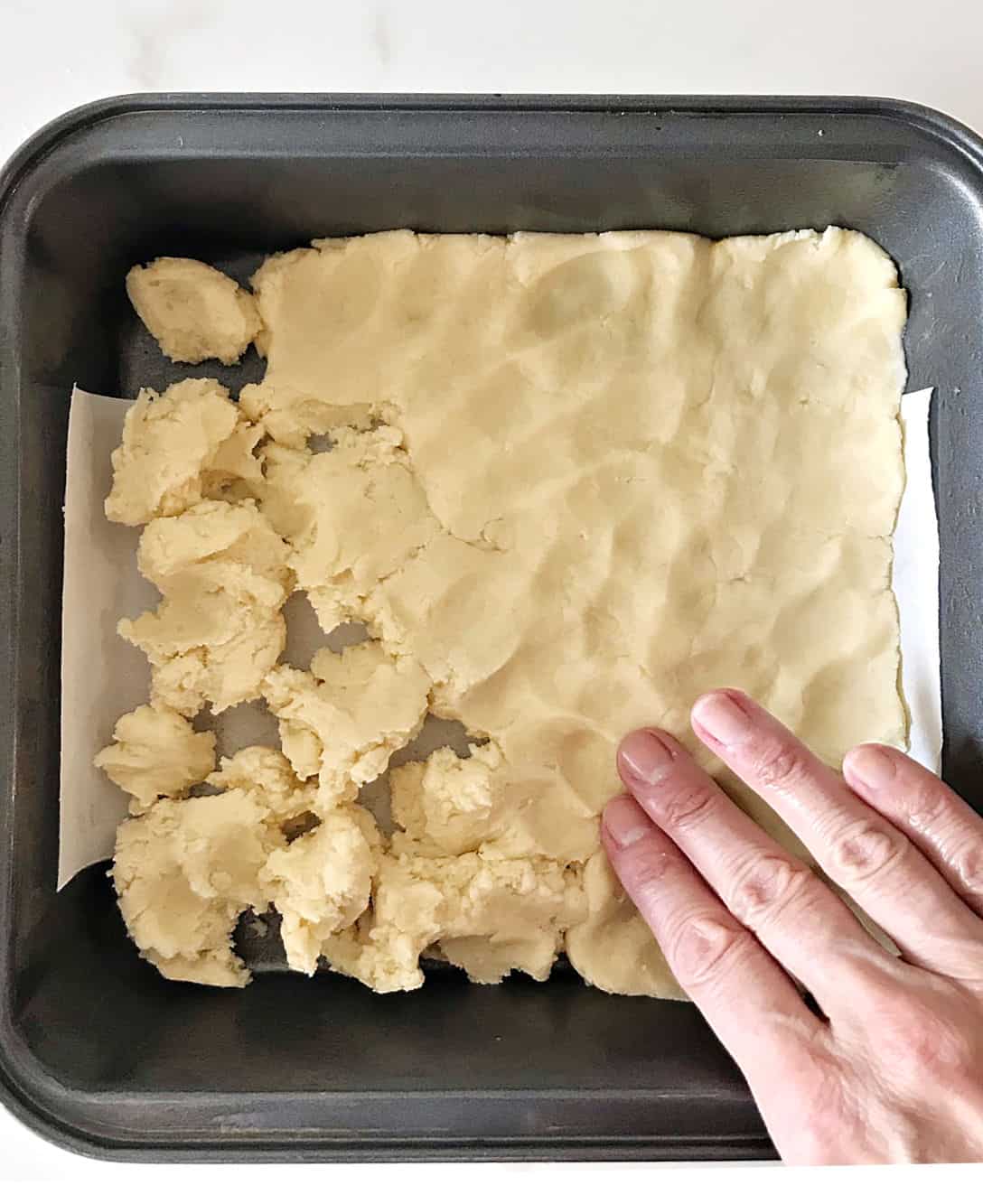 Patting shortbread in a square metal pan with parchment paper.
