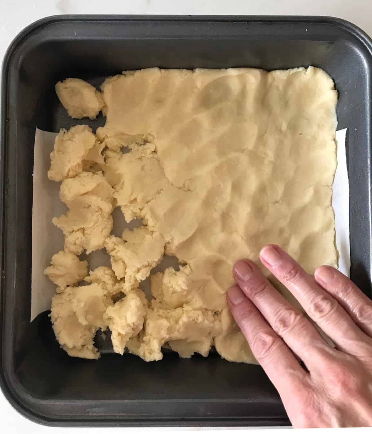 Patting shortbread dough on a metal square pan. 