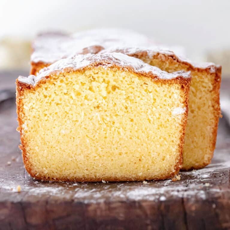 Front view of sliced vanilla pound cake dusted with powdered sugar on a wooden board.