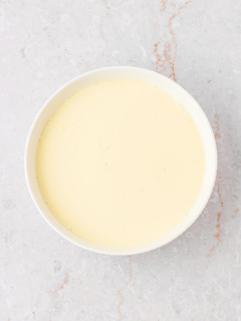 Custard binding sauce for bread pudding in a white bowl. Light gray background.