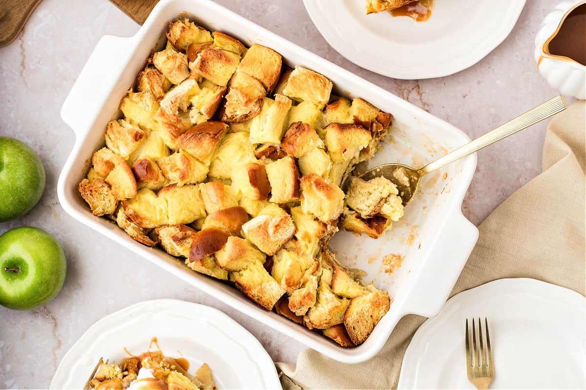 Rectangular white dish with apple bread pudding. White plates, apples. White background.