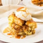 Serving of apple bread pudding with cream and caramel on a white plate.
