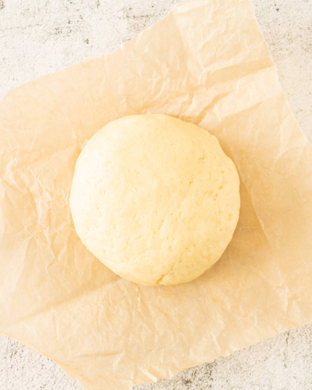 Round ball of pie crust on a beige paper on a light grey surface.