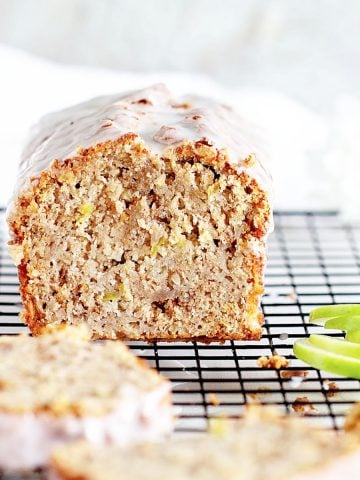 Apple loaf cake on a black cooling rack, slices and cut green apple around.