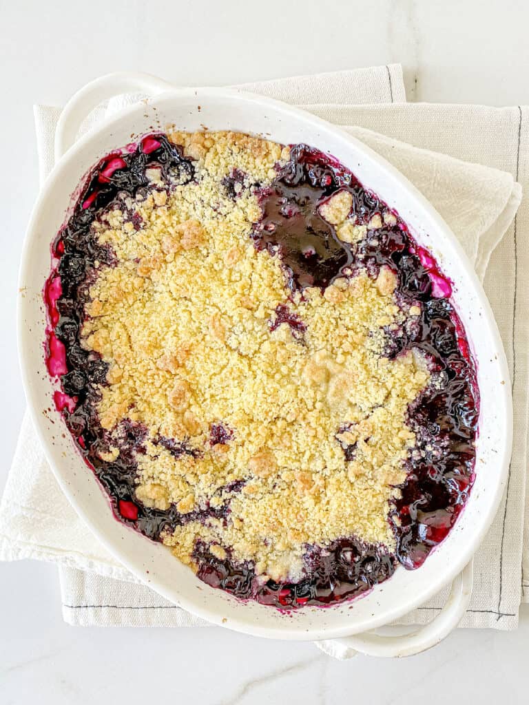 Top view of baked blueberry crumble in an oval white dish on a white surface.