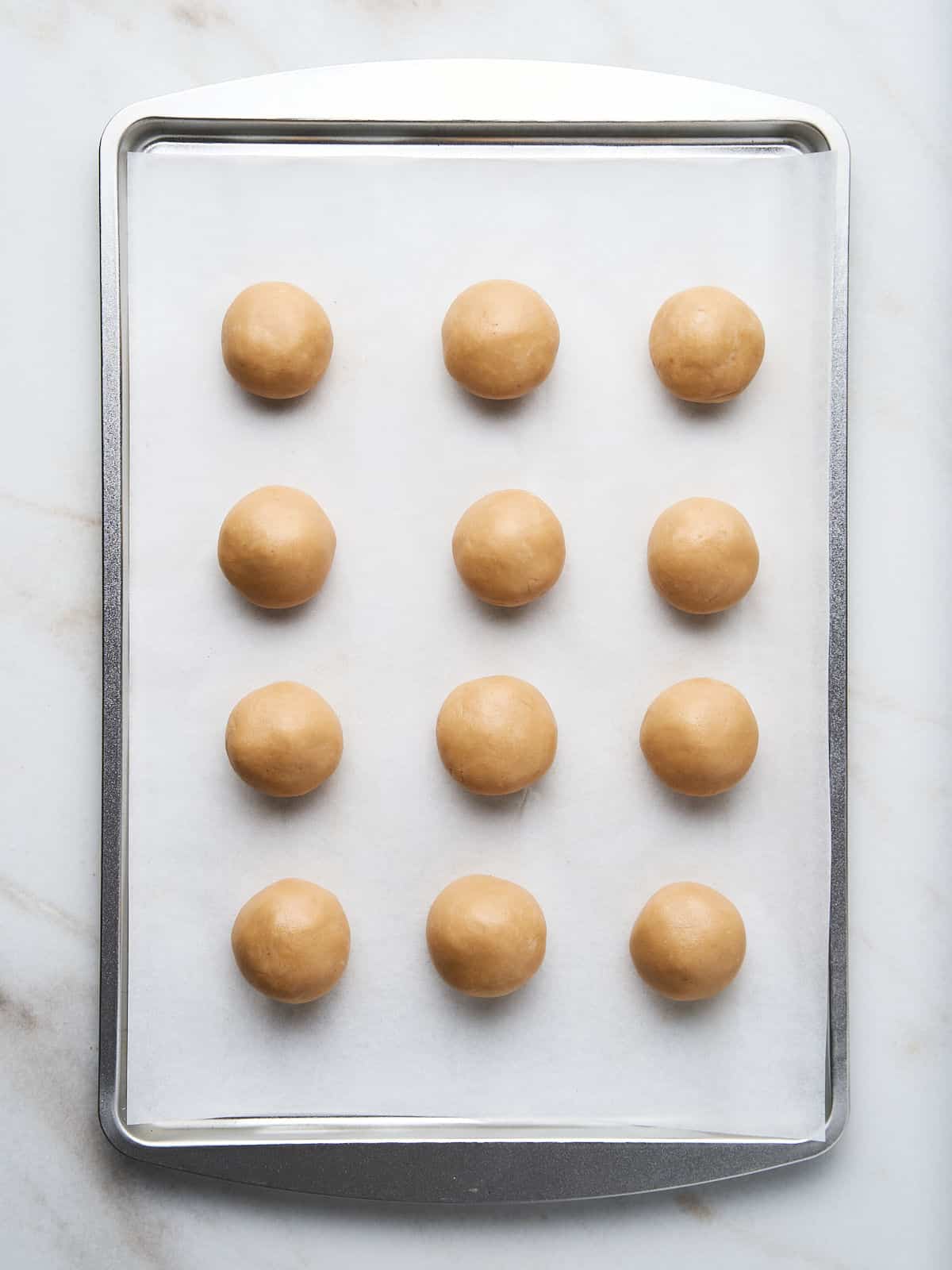 Baking tray with parchment paper and peanut butter balls. White marble surface. .