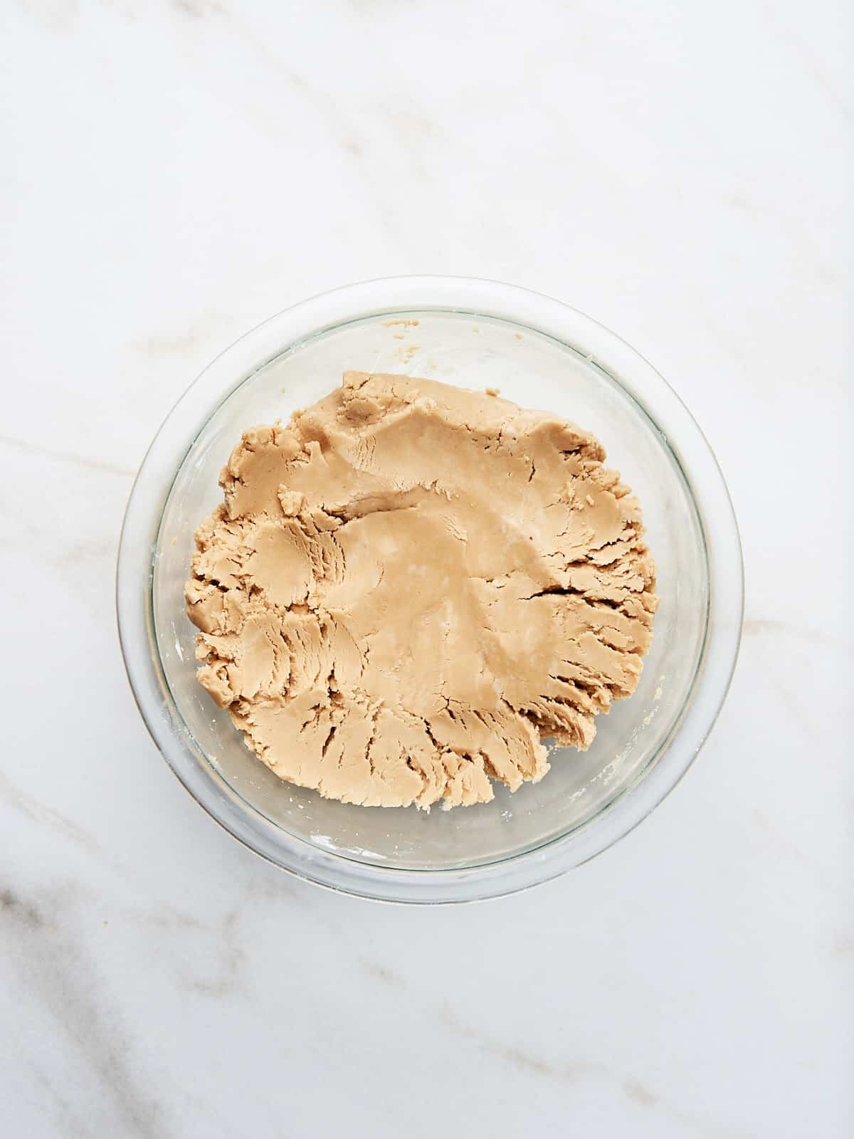 Peanut butter sugar dough in a glass bowl on white marble.