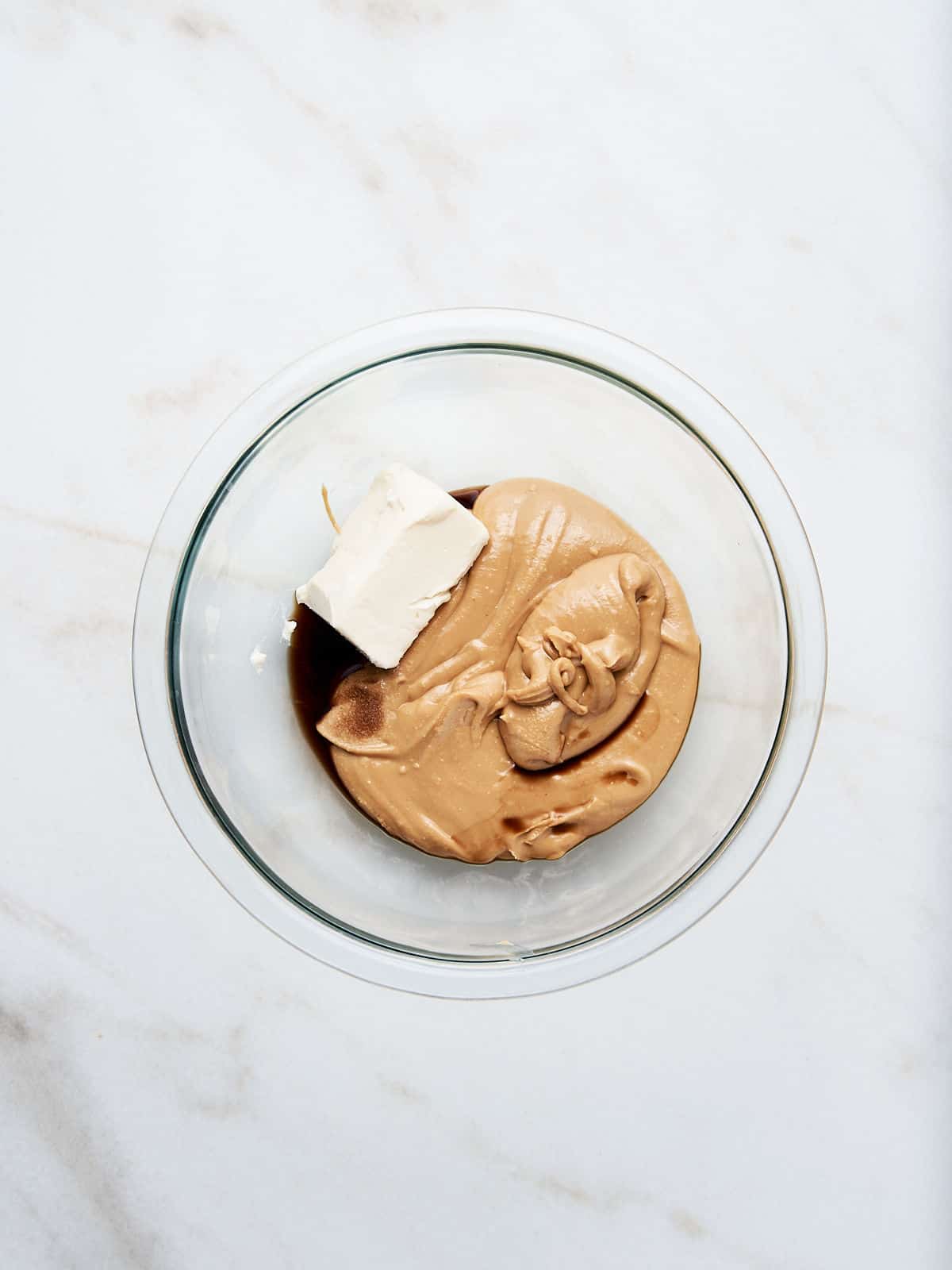 Glass bowl on a white surface with peanut butter, butter, and vanilla.