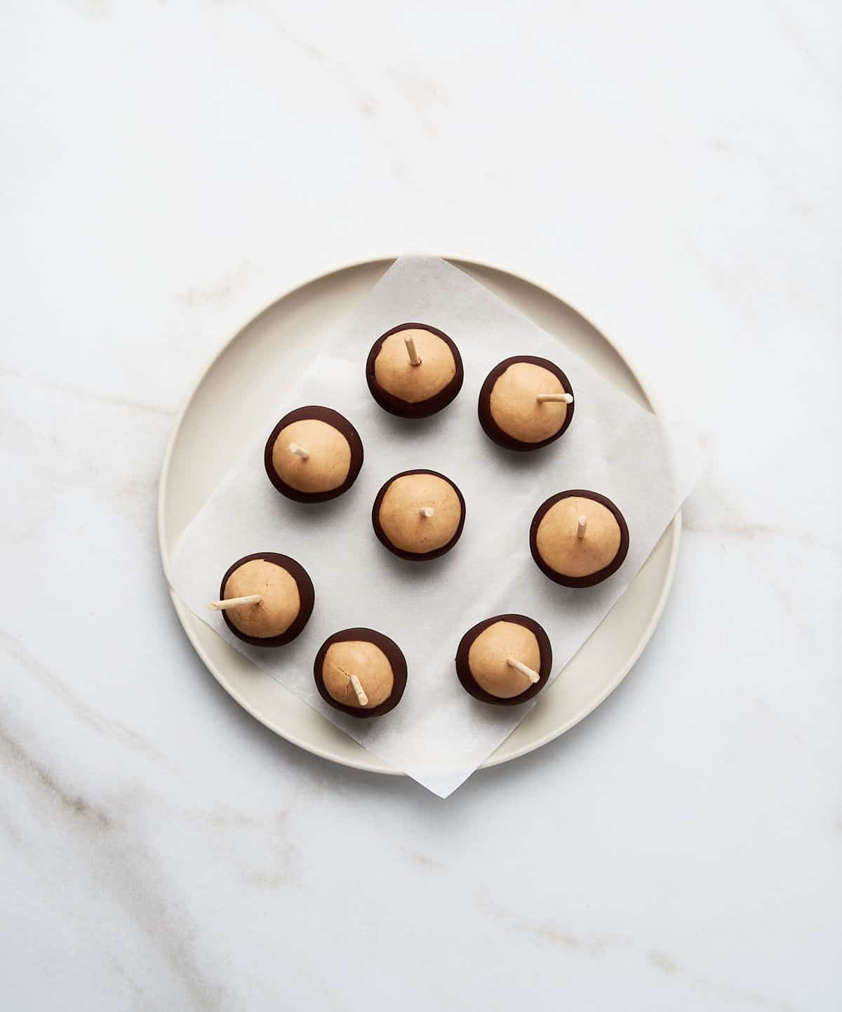 Buckeye candy balls on a whitish plate with parchment paper on white marble. 