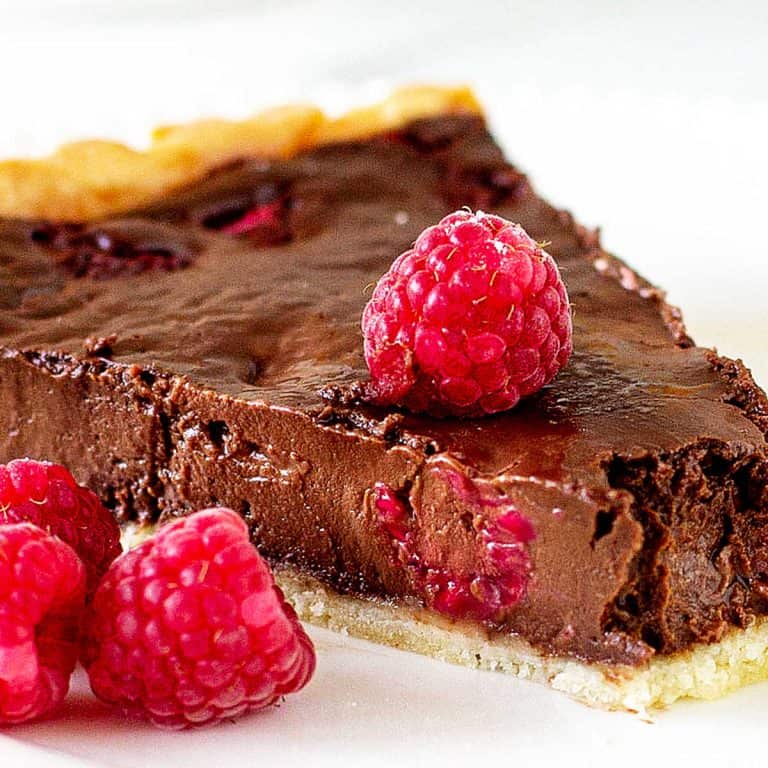 Close up slice of chocolate raspberry tart on a white plate with fresh raspberries.