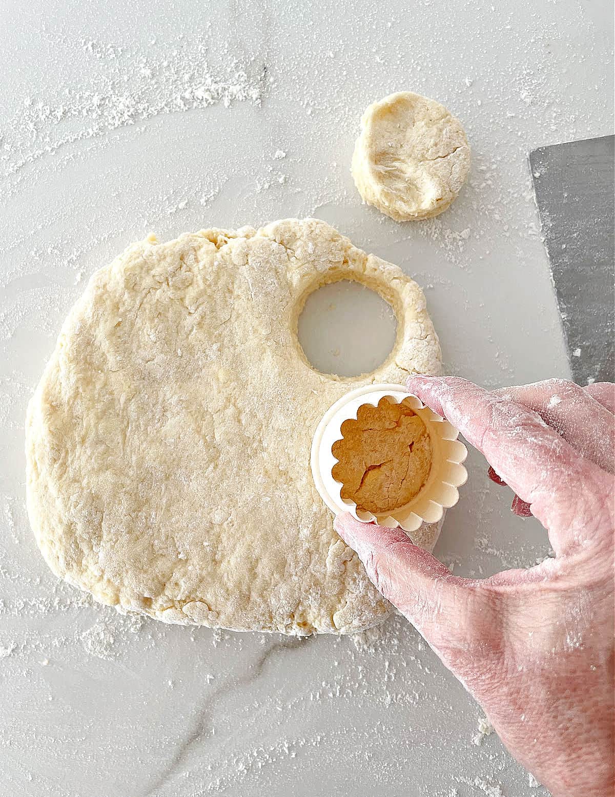 Hand cutting round scones from dough on a white marble surface.